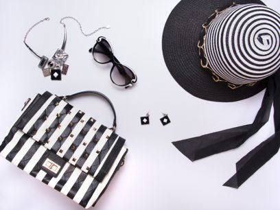 Sombrero de mujer a rayas, gafas, arete, collar, bolso blanco y negro con rayas sobre fondo blanco. endecha plana, vista superior. estilo de moda moderna